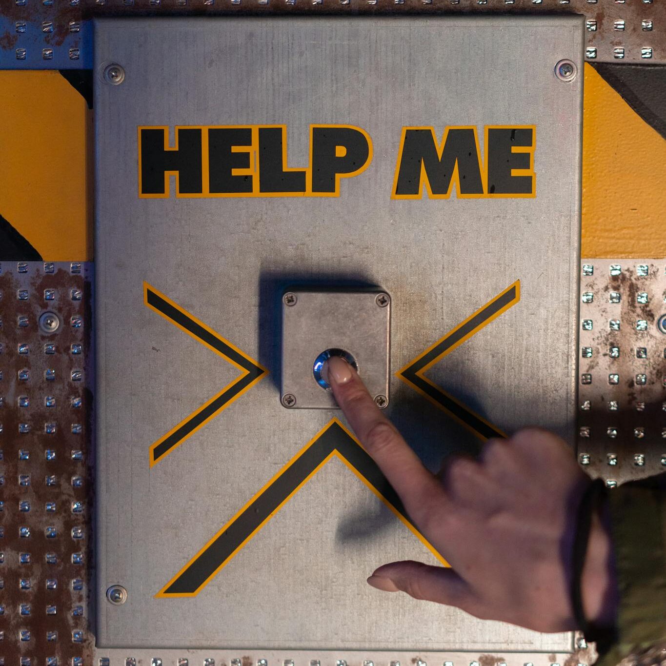 A hand presses an emergency 'help me' button on a metallic panel, evoking sci-fi themes.