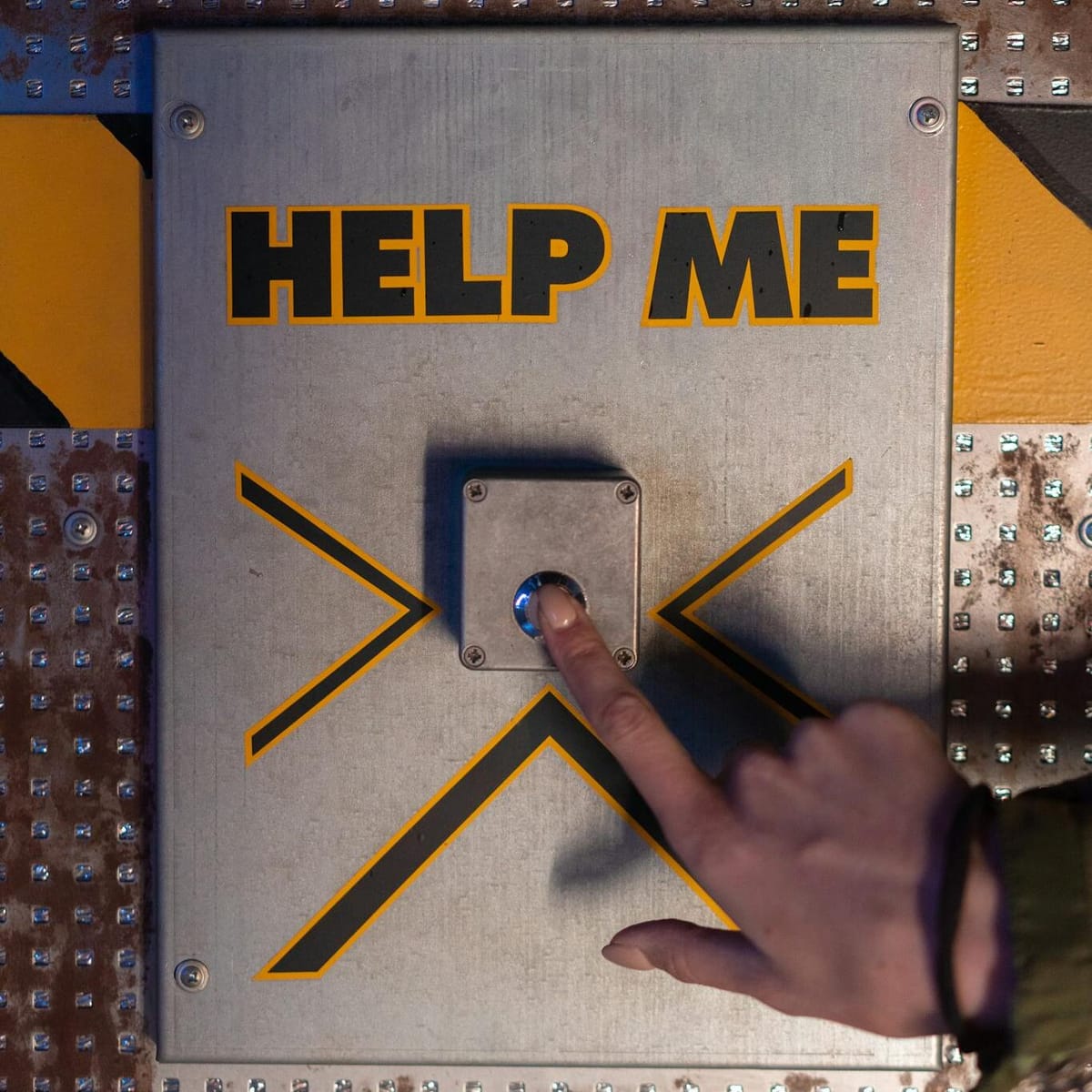 A hand presses an emergency 'help me' button on a metallic panel, evoking sci-fi themes.