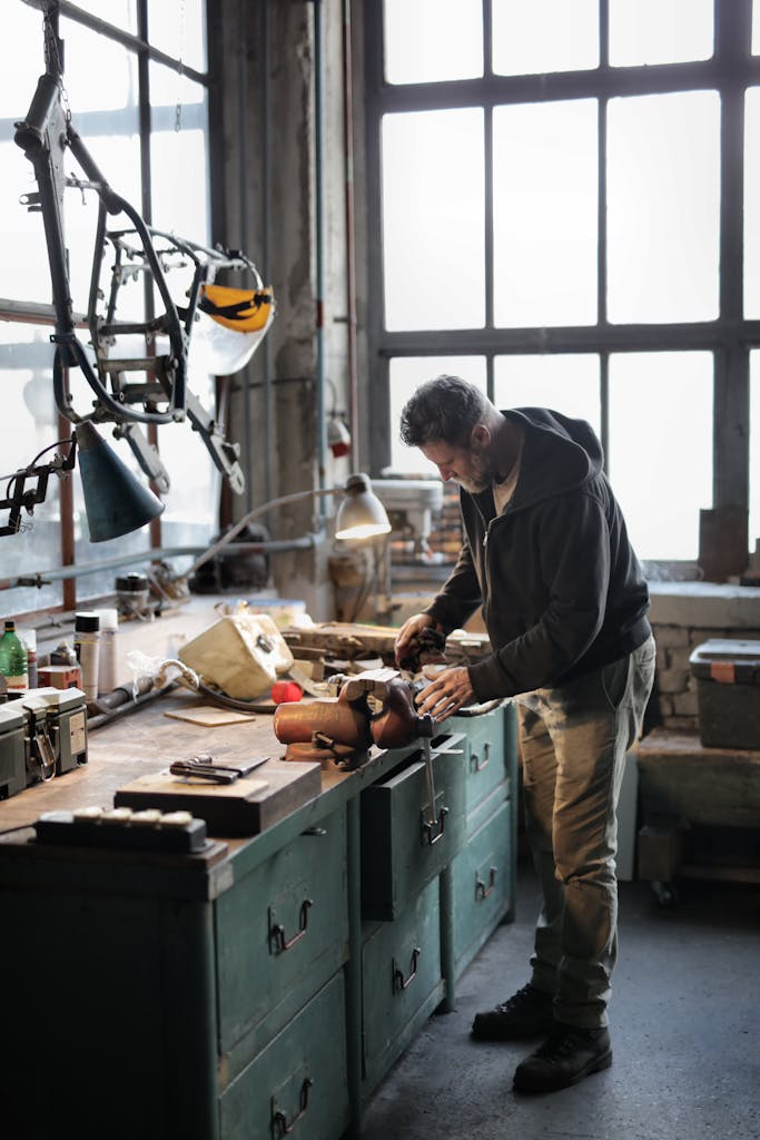 Side view of bearded male master in casual clothes standing at workbench and fixing details with professional metal instrumen