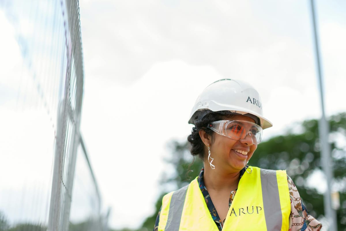 Smiling female engineer in protective gear at an outdoor construction site.