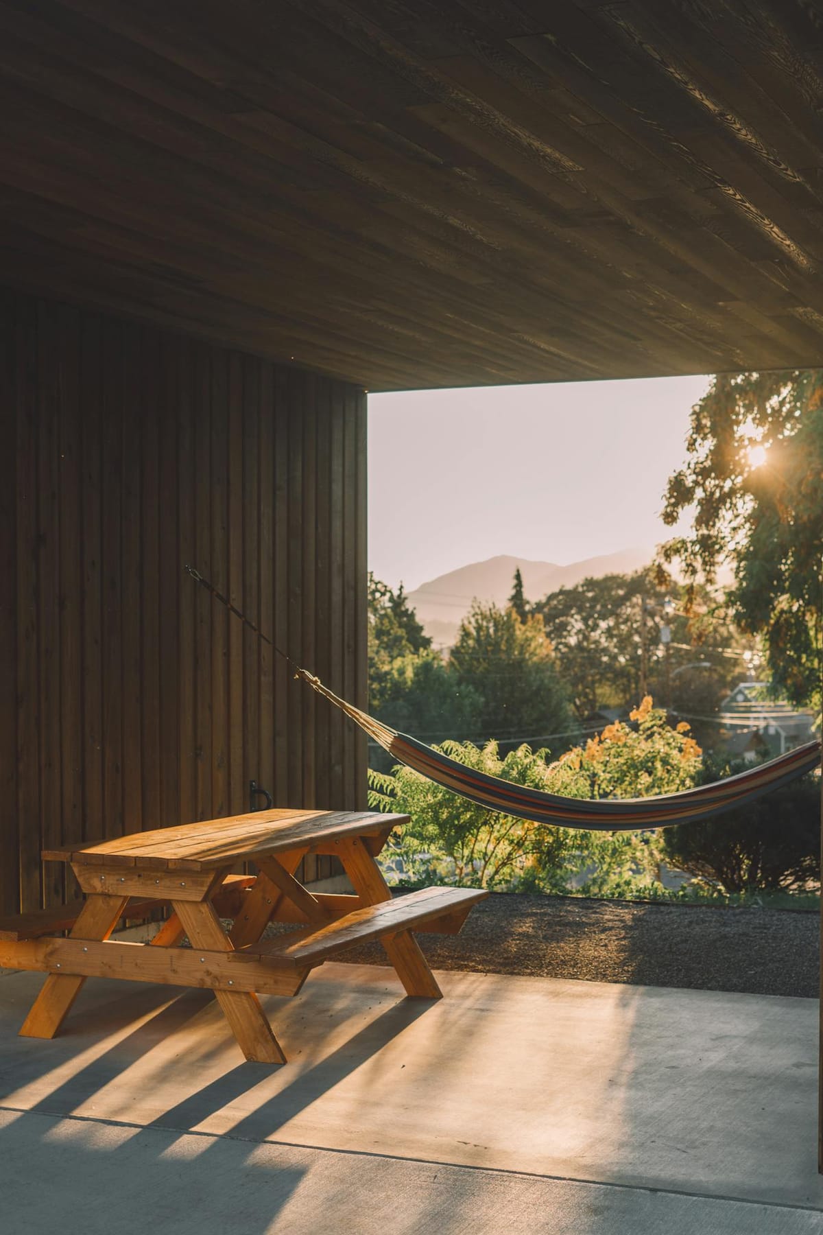 Table with benches on floor on house terrace near greenery trees in countryside in sunlight