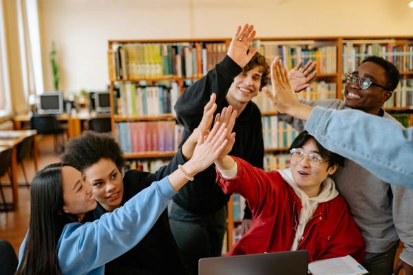 Group of happy students high-fiving in a library setting, celebrating success.