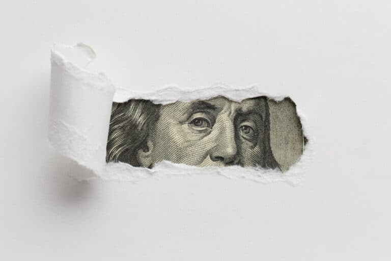 torn paper with money behind it.