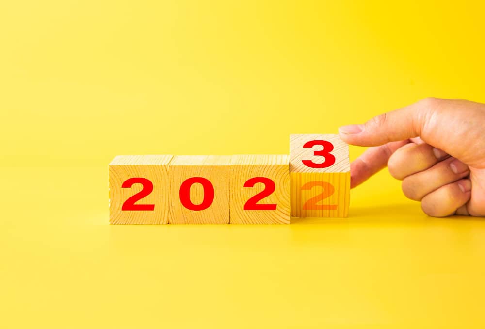 Hand flips wooden cubes with 2022 to 2023 on yellow background