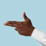 Male hand in white shirt demonstrating a gesture of gun, handgun or pistol isolated on blue background.