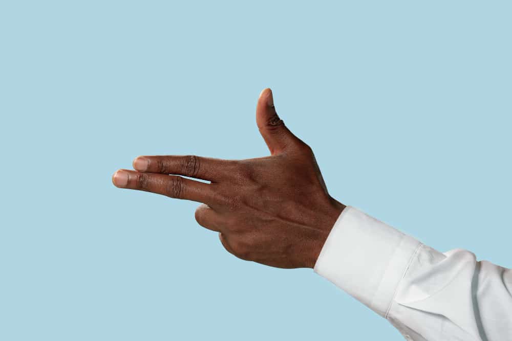 Male hand in white shirt demonstrating a gesture of gun, handgun or pistol isolated on blue background.