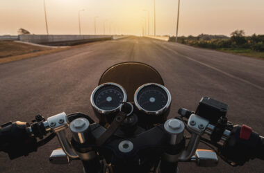 Driver riding motorcycle on an asphalt road in highway at sunset, details of the steering bar.