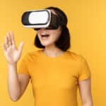 Free photo girl in vr beautiful young asian woman using virtual reality glasses and playing chatting virtually standing over yellow background
