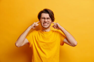 Free photo dissatisfied european man clenches teeth cannot focuse because of noise wears spectacles casual t shirt hears heartbreaking scream isolated over yellow wall. unwilling listen