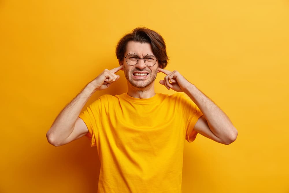 Free photo dissatisfied european man clenches teeth cannot focuse because of noise wears spectacles casual t shirt hears heartbreaking scream isolated over yellow wall. unwilling listen 