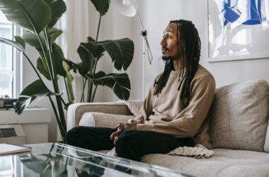 Side view of African American male client sitting on couch and speaking during consulting therapy in modern office with green plant