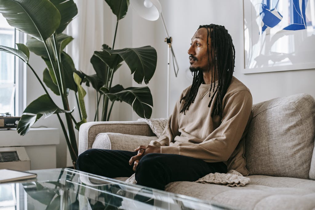 Side view of African American male client sitting on couch and speaking during consulting therapy in modern office with green plant