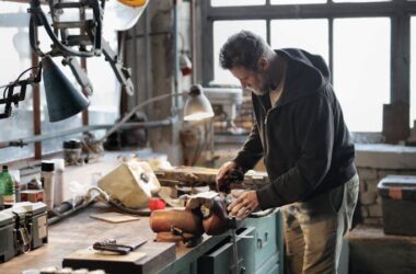 Side view of bearded male master in casual clothes standing at workbench and fixing details with professional metal instrument