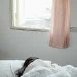 Woman Lying on Bed Near Window