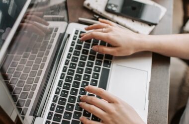 From above of unrecognizable woman sitting at table and typing on keyboard of computer during remote work in modern workspace