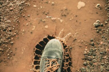 A single boot stepping into a muddy puddle outdoors, creating a splash on a dirt road.