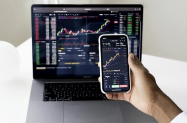 Person checking stock market graphs on laptop and smartphone, focusing on financial data.