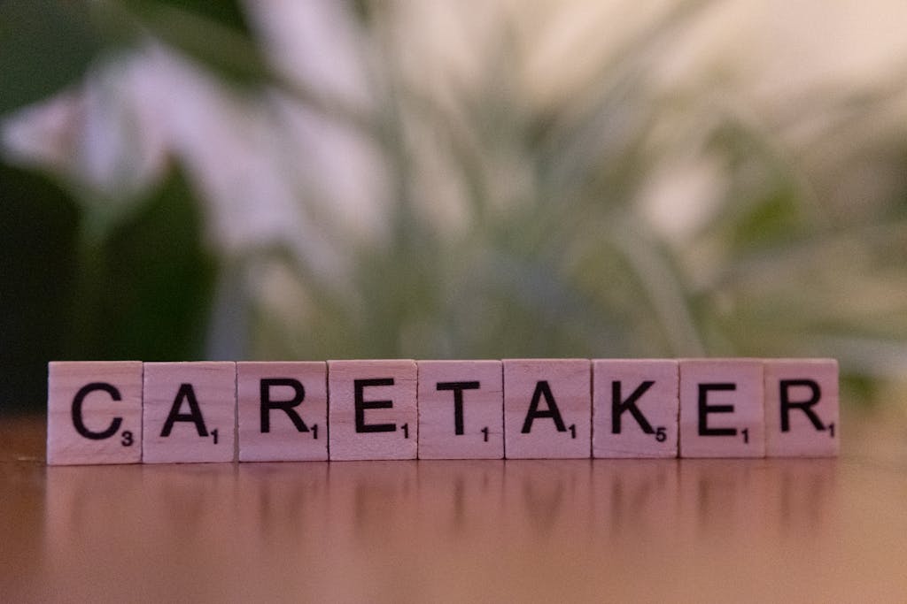 Close-up of Scrabble tiles spelling 'caretaker' on a wooden surface with blurred green background.