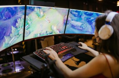A young woman intently gaming on a multi-screen setup, showcasing vibrant gaming visuals.