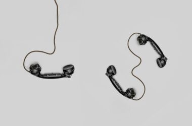 Two vintage black telephone handsets connected by cords on gray background.