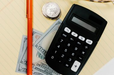 Close-up image of a calculator, pen, and currency on a yellow notepad, symbolizing finance.