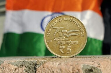 Close-up of a 5 Rupee coin commemorating India's 75th year of independence, set against the Indian flag.